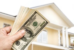 A handful of cash with a house in the background.