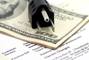 A stack of cash on top of an electric bill with an electrical cord.