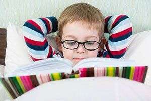 Image of a child reading in bed wearing glasses.