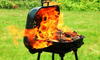 A portable barbeque outdoors with the large flames of a flash fire coming out.
