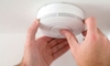 Carbon monoxide and smoke detector attached to the ceiling with hands pushing button on the center
