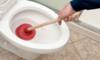 A man using a red plunger to try to unclog a toilet.