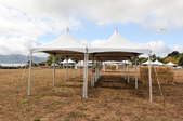 A series of white canopies are set up in the middle of a field for cover.