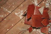 A pile of broken, red ceramic tile on wood subflooring.