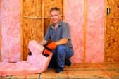 A man preparing to install pink fiberglass insulation in a wall.