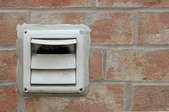 white dryer vent mounted in a brick wall