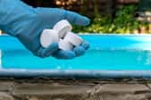 gloved hand holding pool chemicals by water