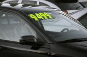 A black car with a price sticker on the windshield.