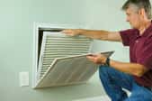 A man checking out an HVAC vent in a wall. 