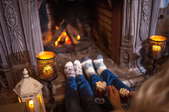 A couple people sitting in front of a fireplace with candles and cups of hot chocolate. 