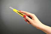 A woman's hand holding up a yellow utility knife.