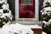 Snow falling on the brick step of a home with a white storm door.