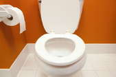 A toilet in an orange bathroom.