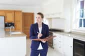 A female realtor standing in a kitchen with a clipboard.