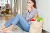 upset barefoot woman on kitchen floor with bag of groceries