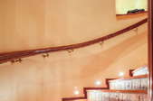 A lit, curved stairway with a handrail mounted on the wall.