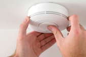 Carbon monoxide and smoke detector attached to the ceiling with hands pushing button on the center
