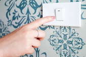 pushing a light switch on a wallpapered wall.