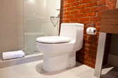 A toilet in a bathroom with a brick wall and a shower stall.