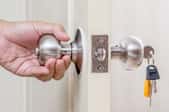 A hand opening a door knob with keys in it.