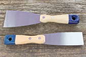 Two putty knives on a rustic wood surface.