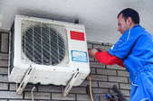 Man on a ladder repairing an air conditioner