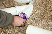 A hand applying purple PVC cement to the inside of a pipe.