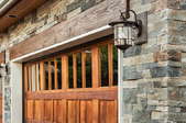A garage door against a stone surrounding with a mounted light.