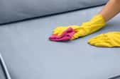 A woman cleans a stain on a couch.
