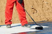 A worker rolling roofing tar on a flat roof.