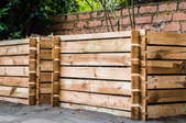 large wooden compost bins by a brick wall