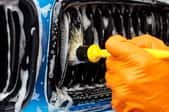 gloved hand cleaning car grille with brush