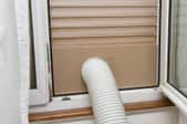 A portable air conditioning unit is set up with the hose venting out a window.