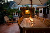 A patio with a long wooden table and lights on it, with chairs on both sides  of the table.