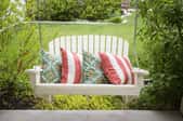White porch swing and throw pillows with yard in the background.