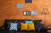 Colorful pillows on a sofa with brick wall in background. 