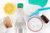 A grouping of homemade cleaning products including an essential oil bottle and a lemon. 