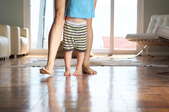 A mom teaching her baby how to walk on wood flooring. 