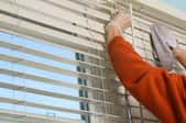 A homeowner wearing gloves and using a cloth to clean their blinds.