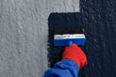 gloved hand painting cement wall with waterproof paint