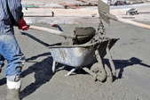 Workers mixing concrete by hand in a wheelbarrow.