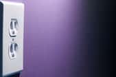 A power outlet on a half-dark, purple wall.