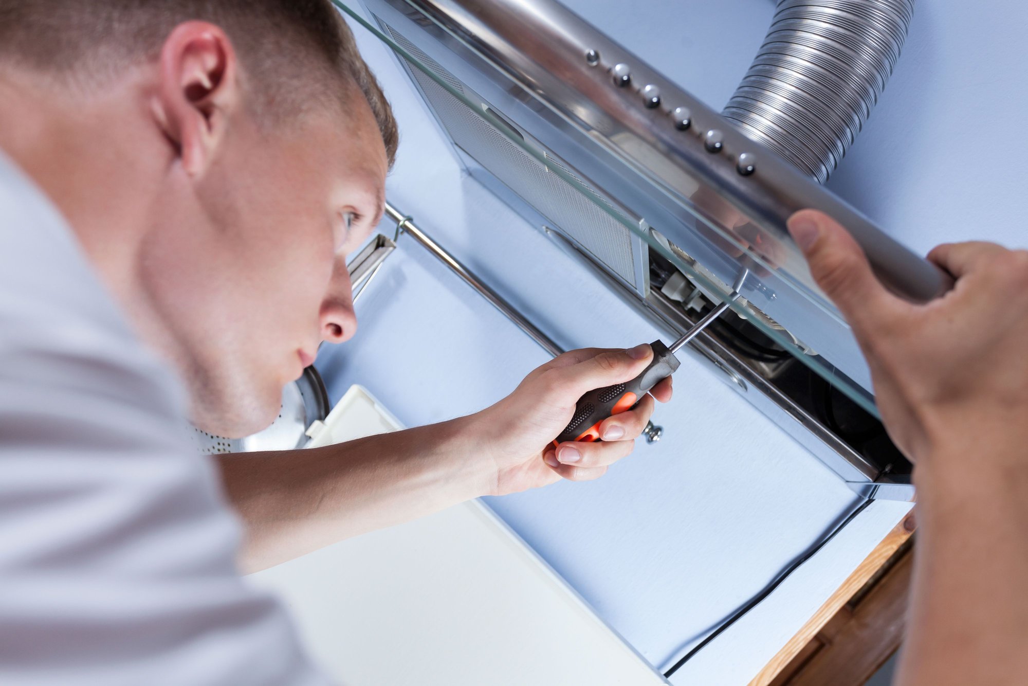 A man works on a cooktop hood.