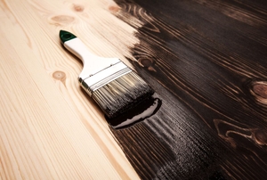 A brush laying on top of a wooden table being varnished.