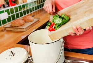 Someone putting kitchen scraps into a small bucket.