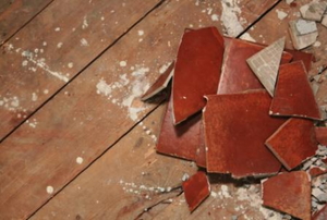 A pile of broken, red ceramic tile on wood subflooring.