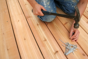 A worker nailing deck boards with a hammer and nails.