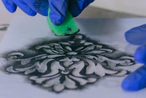 Gloved hands applying paint to a stencil