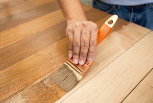 A handyman applying stain to some wood.