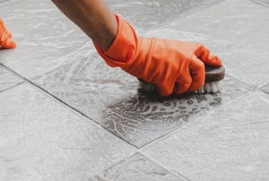 Gloved hands scrubbing a tile floor